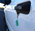 A close-up of a white vehicle door with a black handle and keyhole, showing a key inserted and a hanging keychain tag that reads 