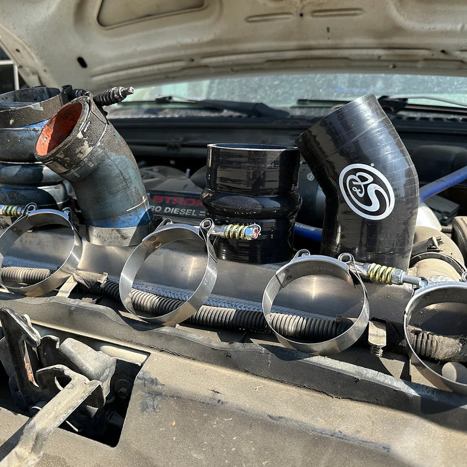 S&B hot side intercooler boots and T-bolt clamps resting on the engine bay of a Ford 6.0L Powerstroke